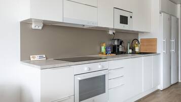 Una cocina moderna con armarios blancos, horno integrado, microondas y cafetera sobre la encimera.