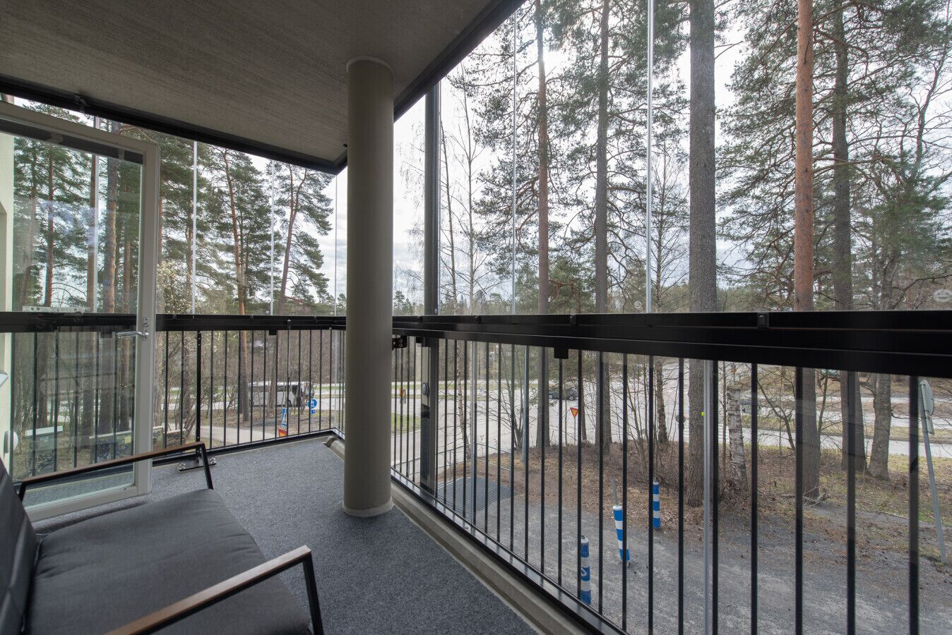 Ein Balkon mit Blick auf hohe Bäume, einem Metallgeländer und einer Betonstütze.