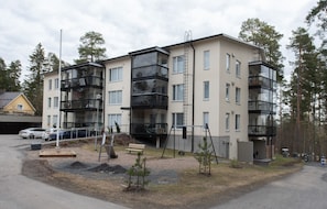 Kerrostalo, jossa on useita kerroksia, parvekkeita, pysäköintialue ja pieni puutarha.