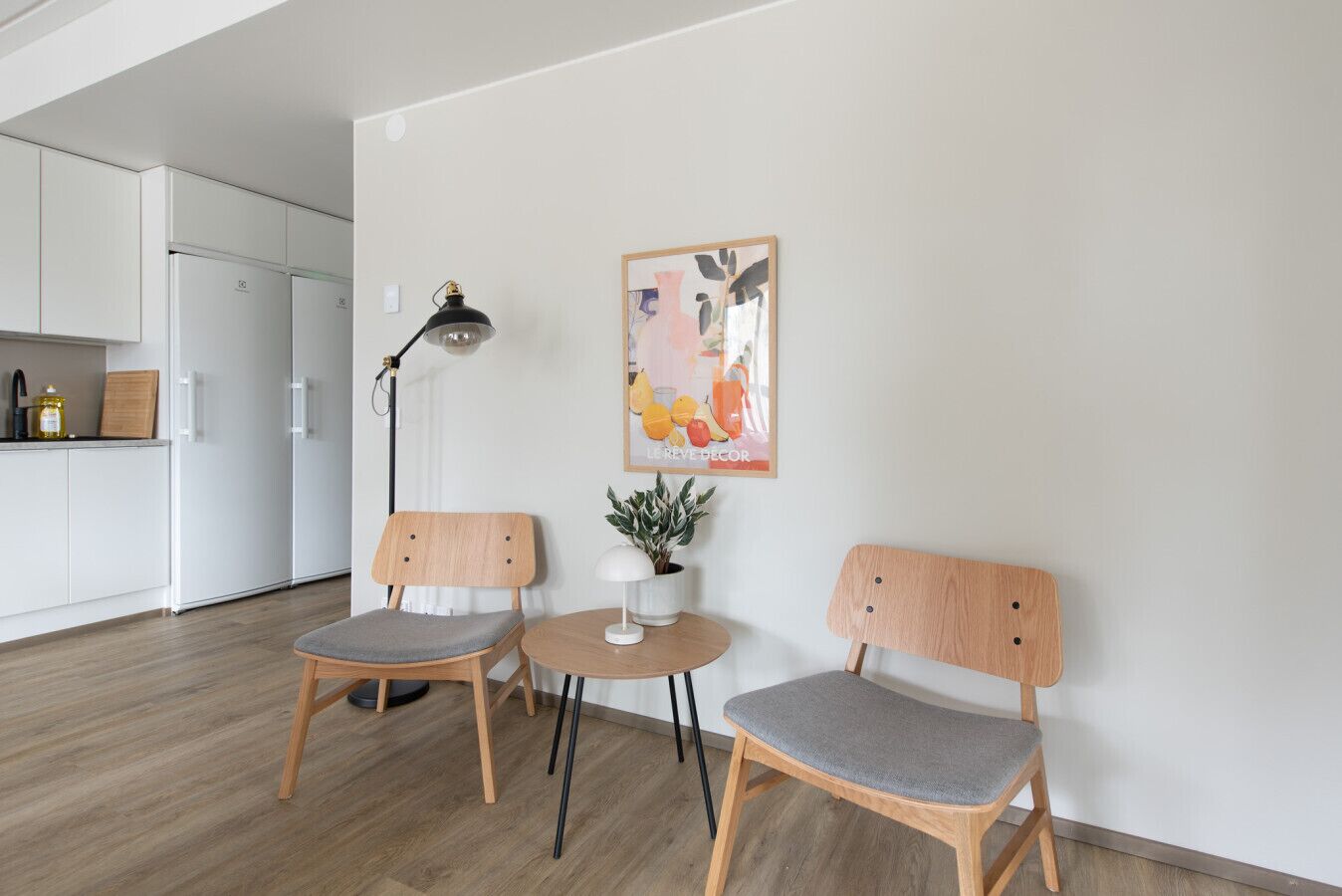 Une cuisine moderne avec des meubles blancs, un lampadaire noir et une affiche accrochée au mur.