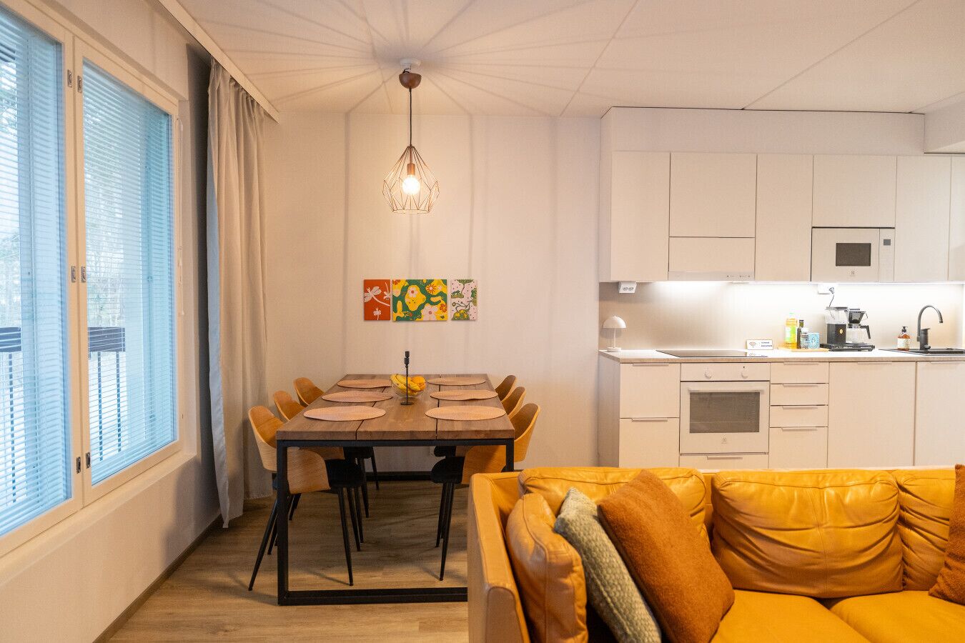 Une cuisine moderne avec des meubles blancs, un coin repas doté d’une table en bois et de chaises jaunes, et un canapé jaune au premier plan.