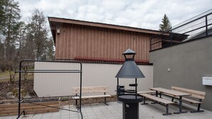 An outdoor patio with a metal grill, wooden benches, and a black trash can. - Beautifully furnished family apartment - parking, sauna, balcony (Jyväskylä)