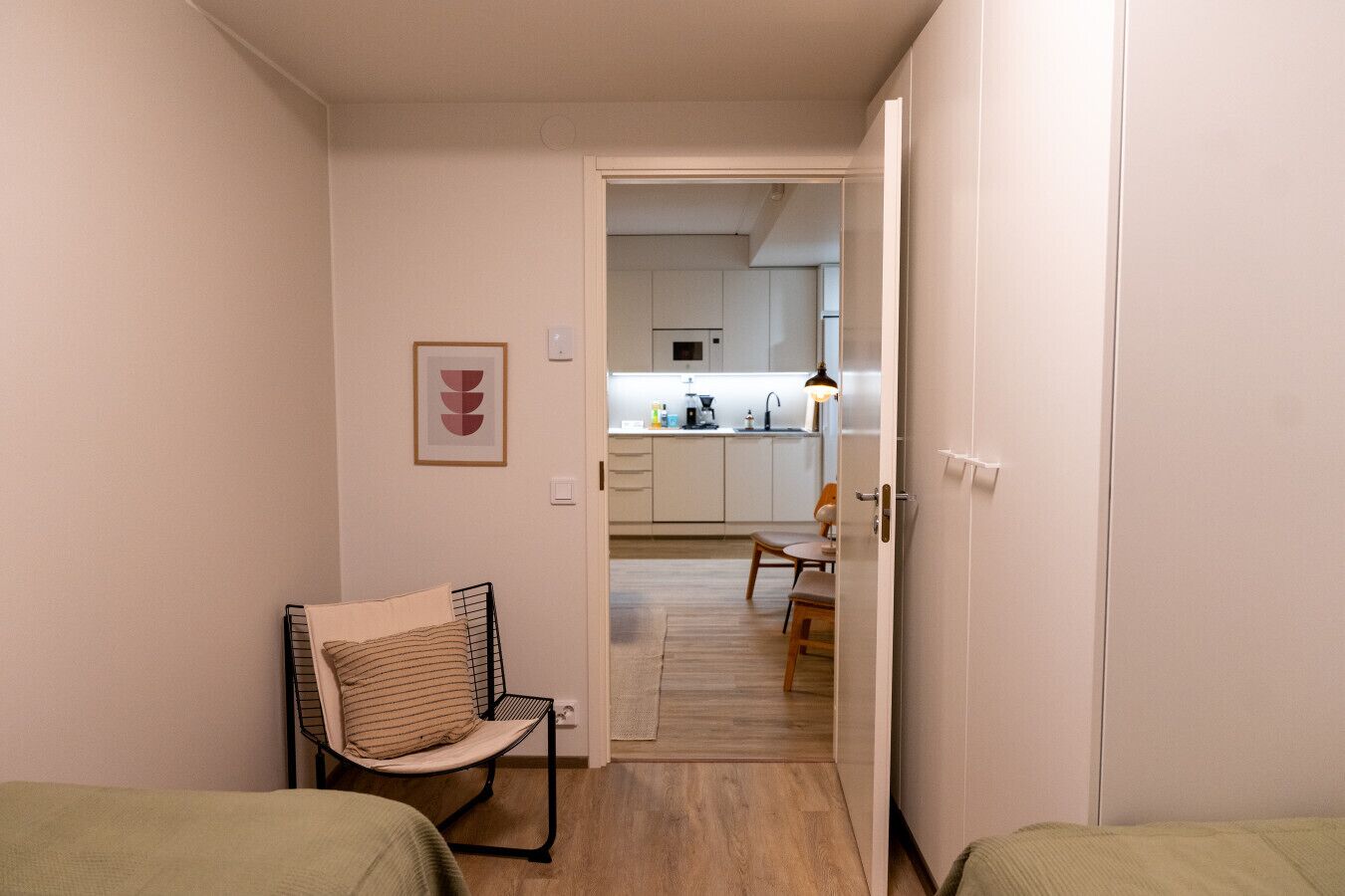 Una habitación pequeña con una cama, una silla y una kitchenette al fondo.