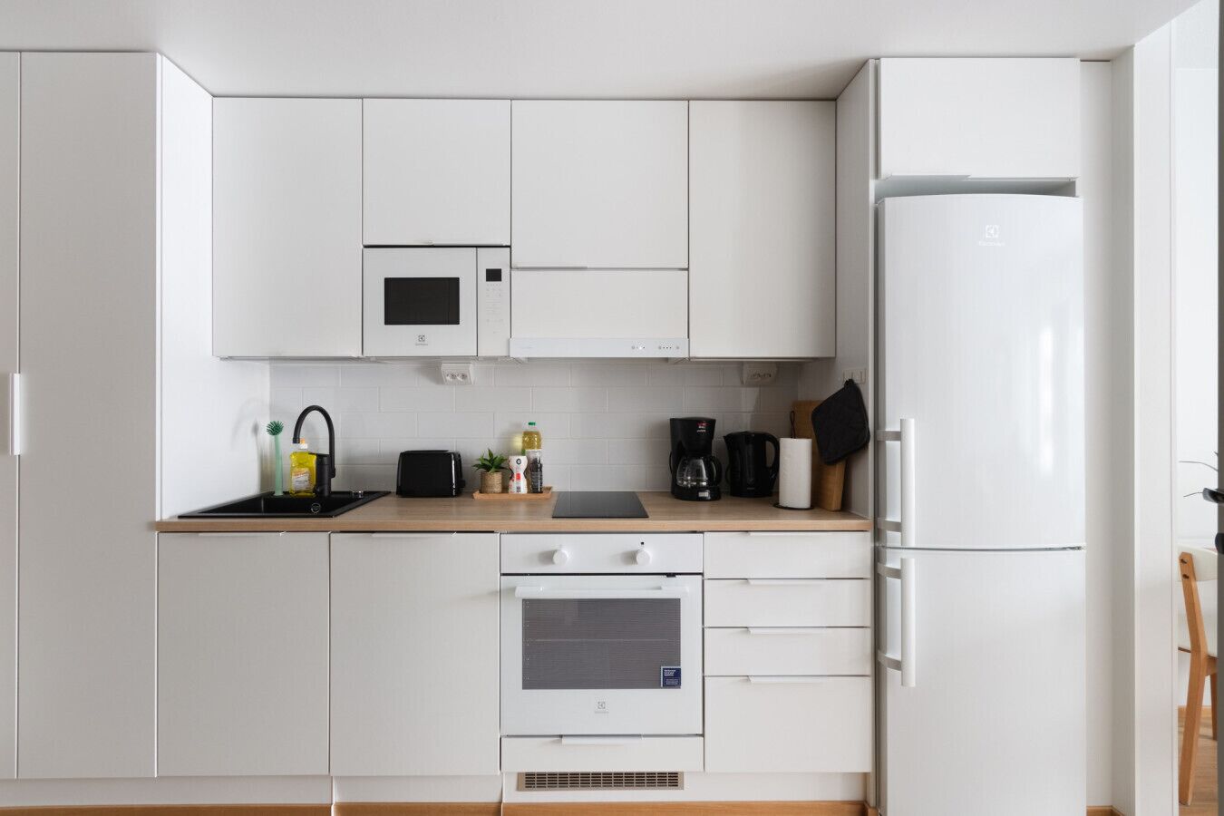 Una cucina moderna con mobili bianchi, un forno a microonde, una macchina da caffè e un frigorifero.