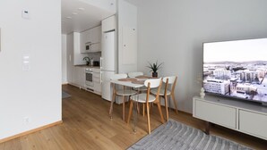Apartamento moderno com área de jantar, cozinha e uma grande tela de TV exibindo uma paisagem urbana.