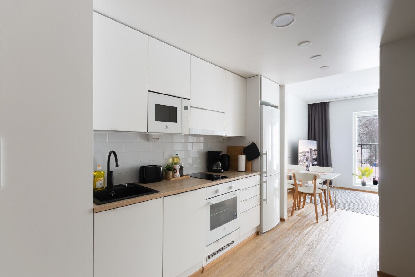 A modern kitchen with white cabinets, a microwave, a sink, and a dining area with a table and chairs.