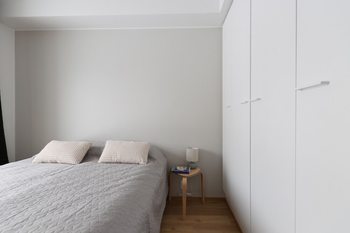 A bedroom with a bed, two pillows, a nightstand with a lamp, and a wardrobe.