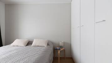 A bedroom with a bed, two pillows, a nightstand with a lamp, and a wardrobe.