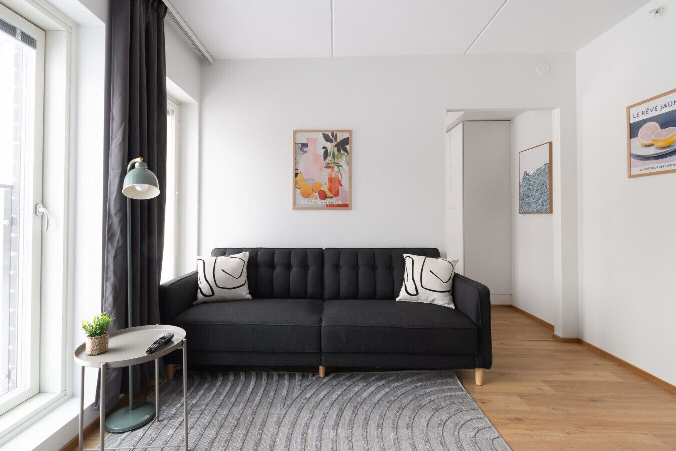 Sala de estar moderna com sofá escuro, mesa lateral pequena, planta em vaso e tapete cinza.