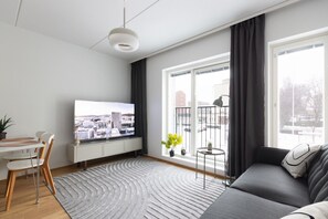 Una sala moderna con televisor de pantalla plana, un sofá, una mesa de comedor con sillas y un amplio ventanal con vistas a edificios.