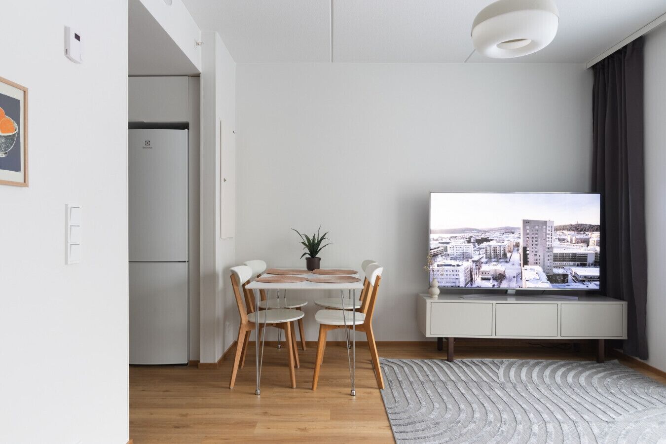 Moderni olohuone, jossa on ruokailutila, sisäänrakennettu televisio ja näkymä kaupunkimaisemaan.