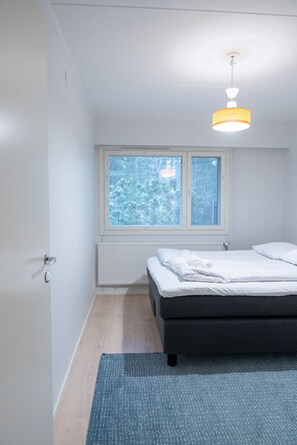 Makuuhuone, jossa on sänky, ikkuna, jossa on sälekaihtimet, patteri ja kattovalaisin.