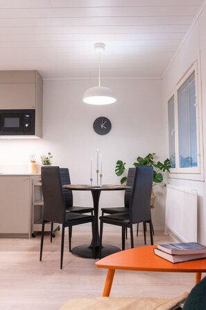 A modern kitchen with a microwave, a dining table with chairs, a clock on the wall, and a window with a view.