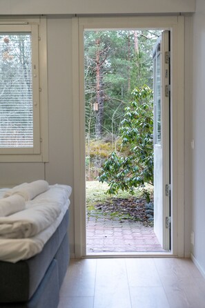 A bedroom with a bed, a window, and an open door leading to a garden.