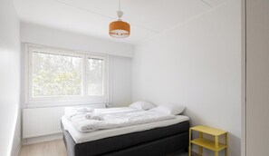 A bedroom with a bed, a window, a radiator, and a yellow shelf.