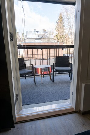 Uitzicht door een glazen deur op een terras met twee stoelen en een tafel.