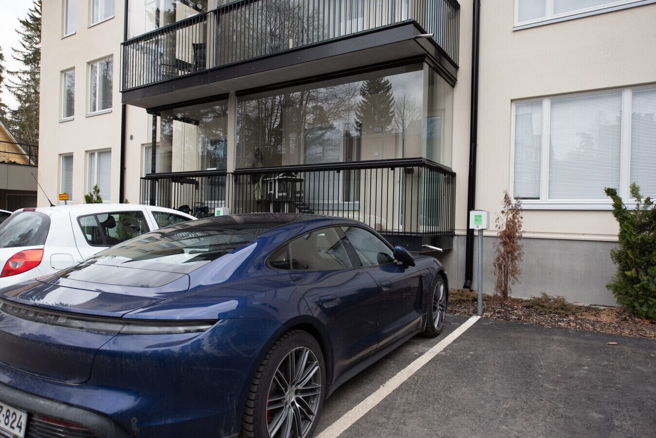 Un edificio moderno con un estacionamiento, un coche deportivo azul y un pequeño árbol.