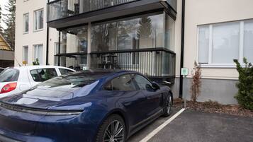 Un edificio moderno con un estacionamiento, un coche deportivo azul y un pequeño árbol.