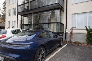Een modern gebouw met een parkeerplaats, een blauwe sportauto en een kleine boom.