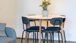 Un comedor con una mesa redonda, cuatro sillas, una lámpara colgante verde y una planta en maceta.
