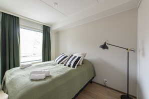 Ein Schlafzimmer mit einem Bett, Kissen, einer Stehlampe und einem Fenster mit Vorhängen.