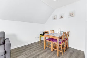 Une pièce comprenant une table à manger, des chaises, un canapé gris et une petite table avec une lampe.