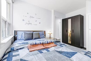 Une chambre avec un lit, un mur orné d’un texte motivant, une armoire et une fenêtre.
