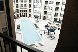 A rooftop pool area with lounge chairs and umbrellas, surrounded by multi-story buildings. - Downtown Houston Skyline Stay, Steps to Daikin Park E (Houston)