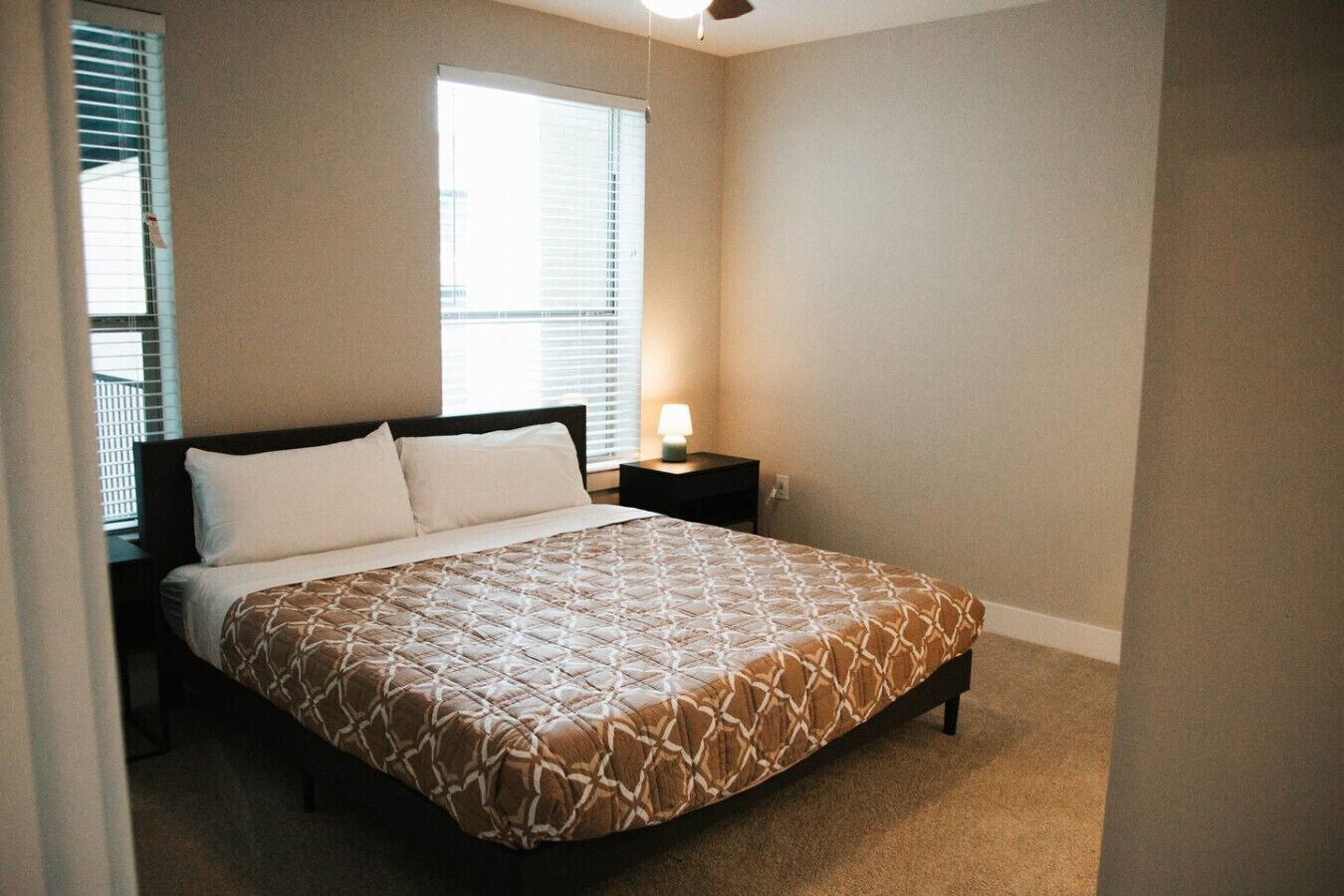 Un dormitorio con cama, mesita de noche, lámpara y ventana con persianas.