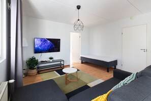 Ein modernes Wohnzimmer mit Flachbildfernseher, einer Bank, einem Sofa, einem kleinen Tisch und einer hängenden Leuchte.
