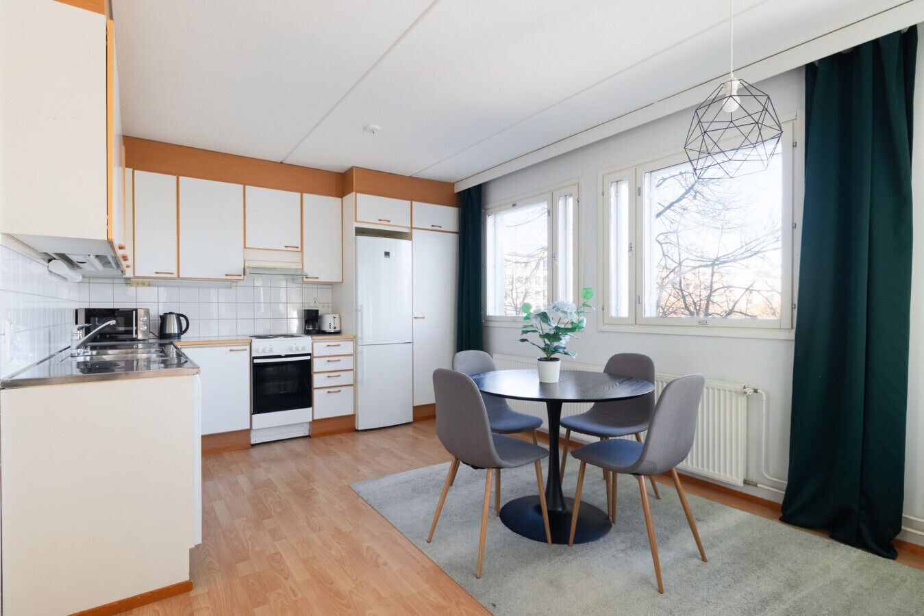 Een moderne keuken met witte kasten, een eettafel met stoelen en een raam met gordijnen.