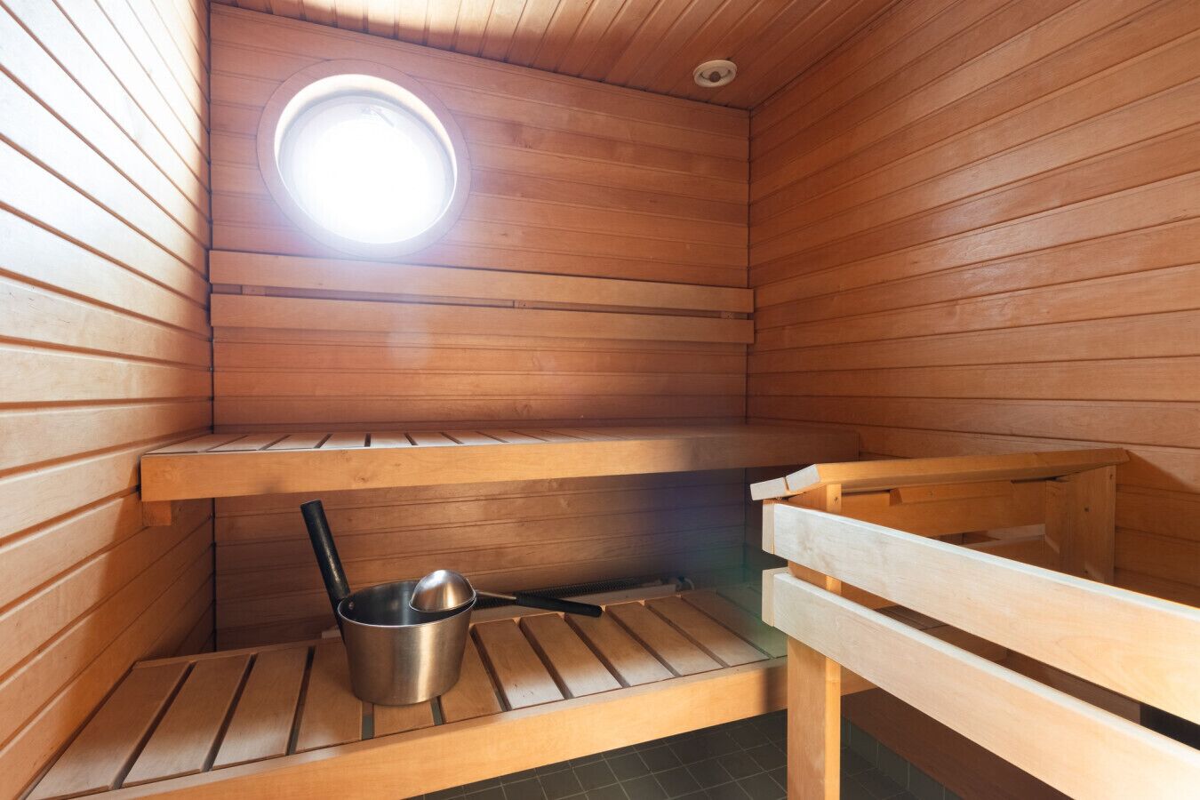 Eine Sauna mit Holzwänden, einer Bank, einem kleinen Tisch und einem Metallbehälter.