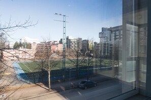 A view of a sports field with a car parked in the foreground, buildings in the background, and a clear sky. - One-bedroom 66m2 apartment with sauna and parking (Helsinki)