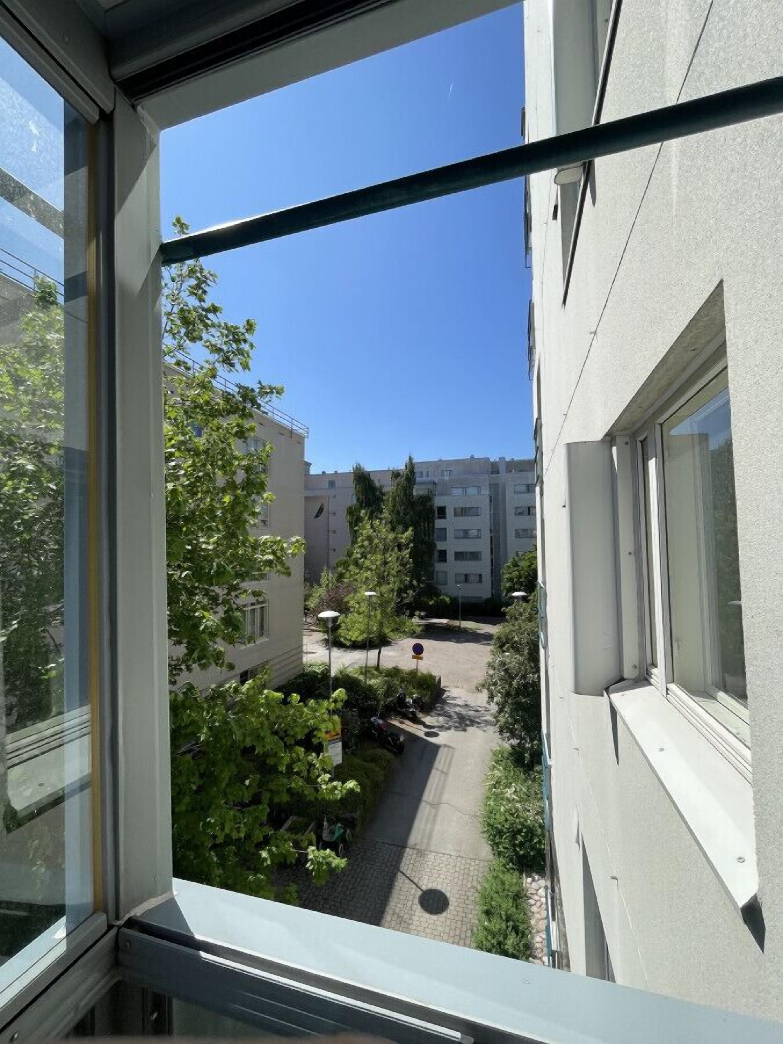 A view from a window overlooking a courtyard with buildings, trees, and a clear sky.