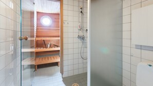 Eine Sauna mit einer Holzbank, einem kleinen Tisch, einer Glastür und einer weiß gefliesten Wand.