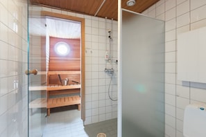 En bastu med en träbänk och ett litet bord, en glasdörr och en vit kakelbeklädd vägg.