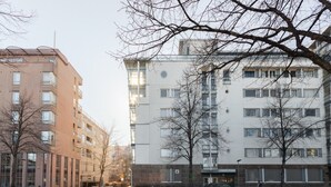 Ein mehrgeschossiges Wohngebäude mit flacher Fassade, großen Fenstern und einem Parkplatz davor.