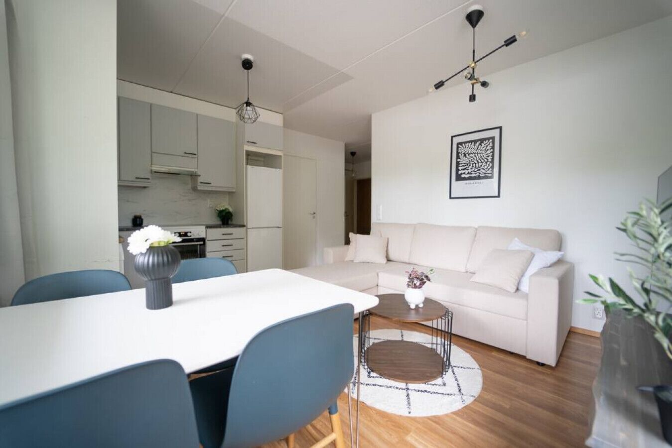 A modern living room with a white sofa, a dining table with chairs, and a kitchen in the background.