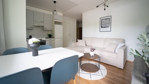 Sala de estar moderna com sofá branco, mesa de jantar com cadeiras e cozinha ao fundo.