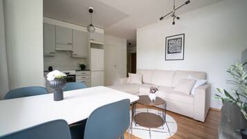 A modern living room with a white sofa, a dining table with chairs, and a kitchen in the background.