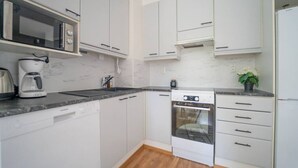 Cozinha moderna com armários brancos, micro-ondas embutido, máquina de café e lava-louças.
