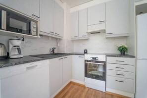 A modern kitchen with white cabinetry, a built-in microwave, a coffee maker, and a dishwasher. - Cozy apartment with sauna and balcony and free parking (Helsinki)