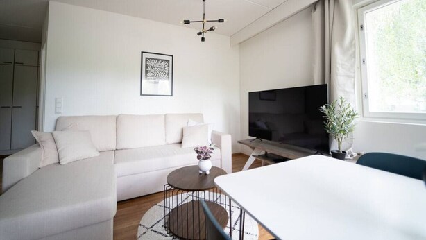 Uma sala de estar moderna com sofá, mesa de centro, televisão e área de jantar.