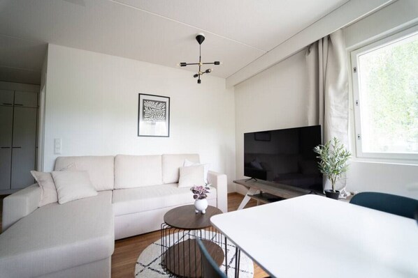 A modern living room with a sofa, a coffee table, a TV, and a dining area. - Cozy apartment with sauna and balcony and free parking (Helsinki)