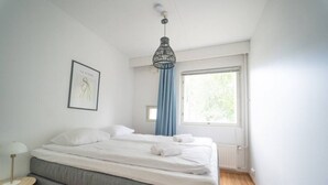 Quarto com cama, mesa de cabeceira, janela com cortinas e luminária suspensa.