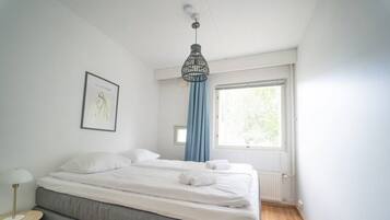 A bedroom with a bed, a bedside table, a window with curtains, and a hanging light fixture.