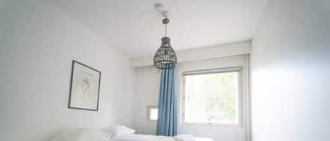 A bedroom with a bed, a bedside table, a window with curtains, and a hanging light fixture.