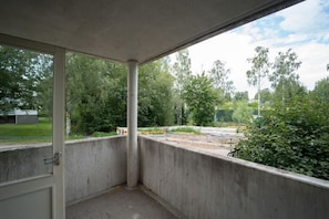 Habitación con piso de concreto, una puerta y vista a una obra en construcción con árboles y una cerca.