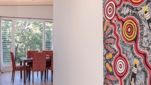 A dining area with a table and chairs, a window with blinds, and a wall with a colorful abstract design. - Paradise Lights 1770 (Seventeen Seventy)