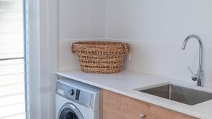 A laundry area with a washing machine, a sink, and a woven basket on the countertop. - Paradise Lights 1770 (Seventeen Seventy)